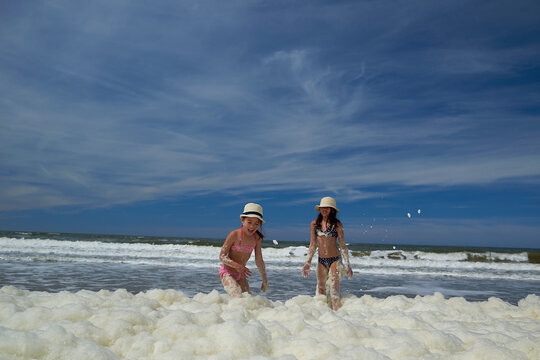 Happy sisters playing in sea foams at beach against sky