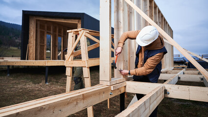 Man worker building wooden frame house on pile foundation. Carpenter hammering nail into wooden...