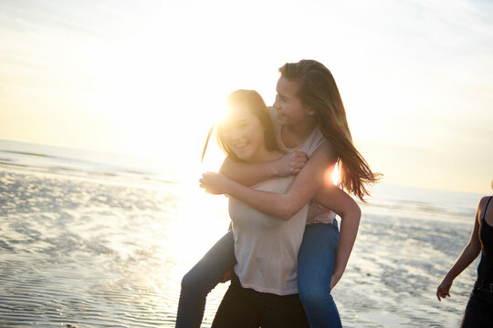 Happy teenage girl piggybacking friend at beach