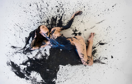 view from above to graphic image of young artistic abstract painted nude sexy woman with black paint, lying on the black and white designed floor in the studio