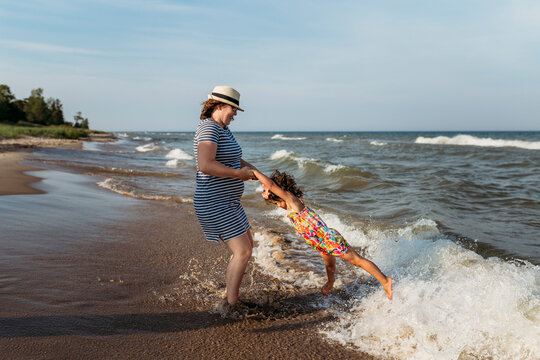 Playful mother spinning daughter at beach against sky