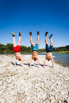 Shirtless friends doing handstand at lakeshore against clear sky