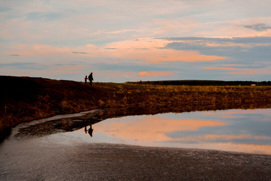 Mother and son walking at lakeshore against cloudy sky during dusk