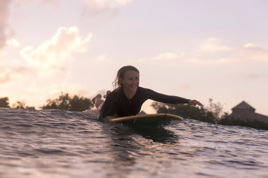 Happy woman lying on surfboard while swimming on sea against sky during sunset