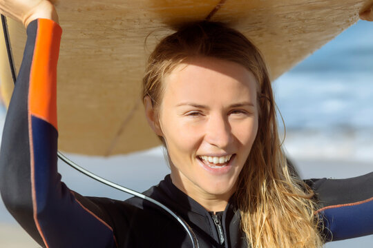 Portrait of cheerful woman carrying surfboard on head at beach