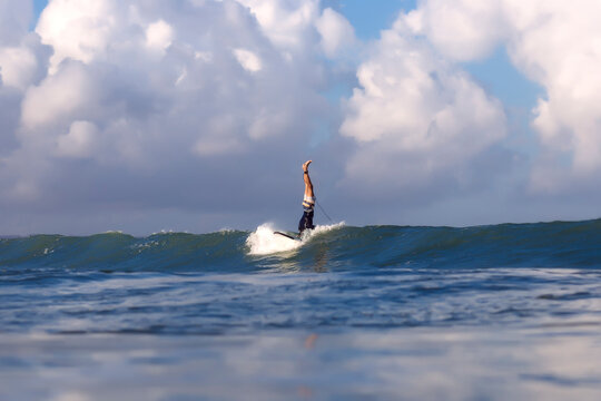 Low section of surfer doing stunts on surfboard against cloudy sky