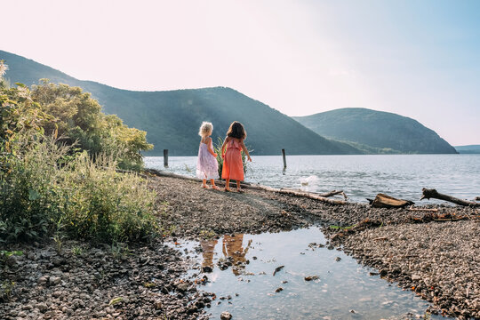 Rear view of friends throwing stones in lake while standing against mountains and clear sky