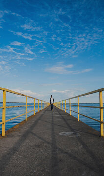 Rear view of boy walking on pier over river against cloudy sky