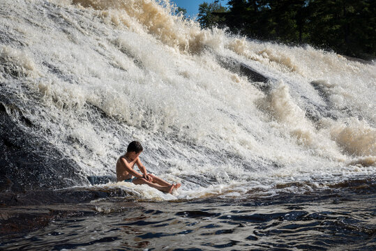 Carefree shirtless boy sitting against waterfall in lake