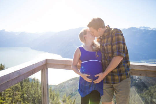 Couple kissing while standing against mountains at observation point during sunny day