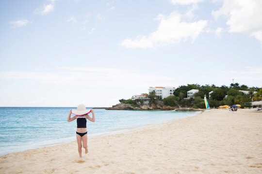 Girl holding hat while walking against sea and sky at beach