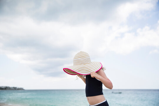 Side view of girl holding hat while standing against sea and cloudy sky at beach