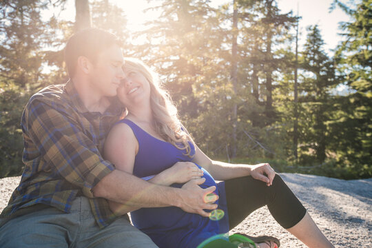 Man touching pregnant woman's stomach while sitting against trees during sunny day
