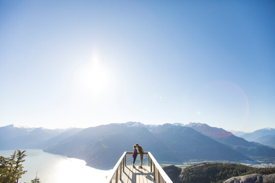 High angle view of couple kissing while standing against mountains and clear sky at observation point during sunny day