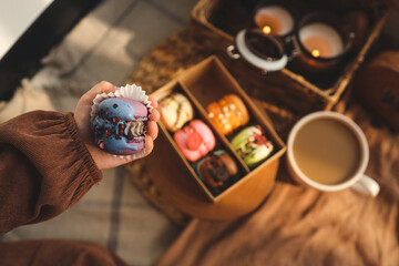 Girl holding a macaron in her hand, with a box of assorted macarons in the background in a cozy home atmosphere