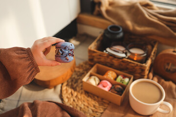 Girl holding a macaron in her hand, with a box of assorted macarons in the background in a cozy home atmosphere