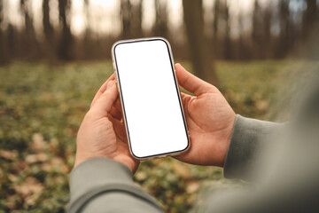Hand holding phone with blank screen taking photo or selfie in the forest. There is no signal. The...
