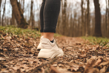 Close up of a womans legs running in the forest. Sport shoes. Trees and leaves in background. Active and healthy lifestyle concept
