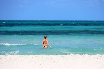 Fototapeta na wymiar Girl in black bikini going to swim in blue sea water. Beach vacation on Caribbean islands