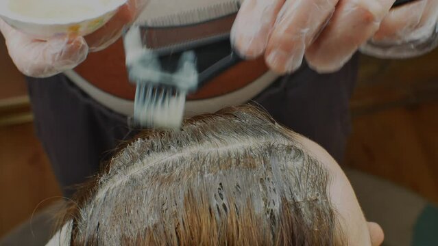 Woman dyes her hair in a beauty salon. A man hairdresser paints over the gray hair roots on the head of a woman client. The concept of hair coloring in a beauty salon
