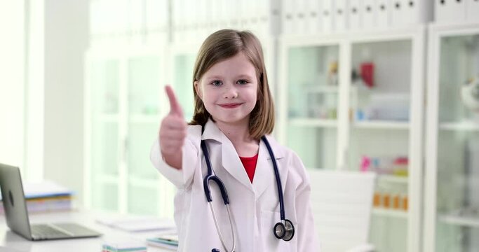 Little girl in medical gown with stethoscope showing thumbs up in clinic 4k movie slow motion
