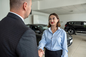 smiling car salesman shakes the hand of a brunette who wants to buy a car.