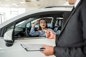 Young female business client talking with a sales man in a car showroom
