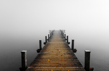 Jetty in the fog. Mystical foggy landscape at the lake. Morning fog in autumn.	