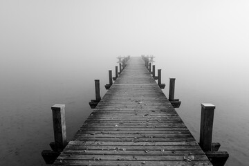 Jetty in the fog. Mystical foggy landscape at the lake. Morning fog in autumn.	