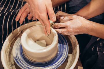 Photo from above. The hands of a man and a woman make a clay vase on a machine using an apparatus. Dating concept