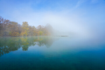 Jetty at the lake in the fog. Misty landscape in the morning. Idyllic nature by the water. Rest and relaxation.
