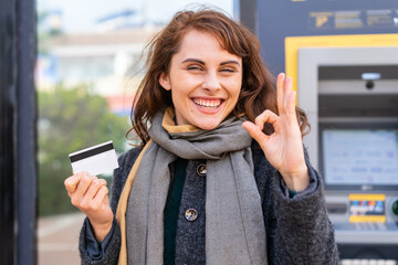 Brunette woman holding a credit card at outdoors showing ok sign with fingers