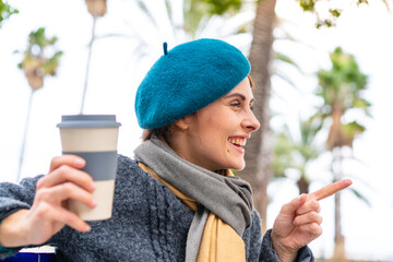 Brunette woman holding a take away coffee at outdoors pointing to the side to present a product