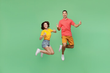 Full body satisfied happy fun cool young couple two friends family man woman wear basic t-shirts together showing thumb up like gesture isolated on pastel plain light green background studio portrait.