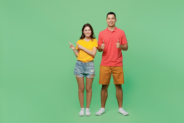 Fototapeta premium Full body young couple two friends family man woman wear basic t-shirts together point index finger aside indicate on workspace area copy space mock up isolated on pastel plain light green background.