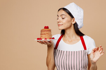 Young housewife housekeeper chef baker latin woman wear striped apron toque hat hold pancakes on...
