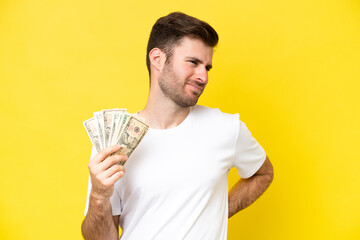 Young caucasian man taking a lot of money isolated on yellow background suffering from backache for having made an effort