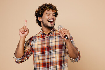 Young smiling happy Indian man wear brown shirt casual clothes sing song in microphone point index...