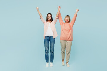 Full body happy elder parent mom with young adult daughter two women together wearing casual clothes raise up hands do winner gesture clench fist isolated on plain blue background. Family day concept.