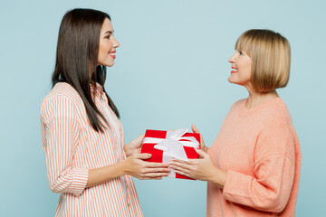 Side view smiling elder parent mom with young adult daughter two women together wear casual clothes hold give present box with gift ribbon bow isolated on plain blue background. Family day concept.