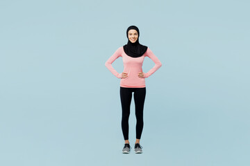 Fototapeta na wymiar Full body fun young arabian asian muslim fitness trainer sporty woman wear pink abaya hijab spend time in home gym stand akimbo isolated on plain blue background studio. Workout sport fit abs concept.