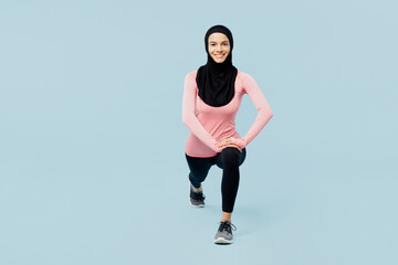 Fototapeta na wymiar Full body happy young asian muslim fitness trainer sporty woman wear pink abaya hijab spend time in gym look camera do squates isolated on plain blue background studio. Workout sport fit abs concept.