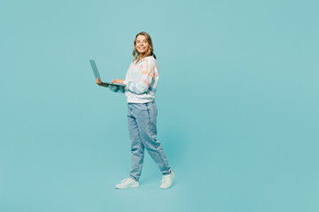 Full body side view smiling cheerful happy young woman wears striped hoody hold use work on laptop pc computer isolated on plain pastel light blue cyan background studio portrait. Lifestyle concept.