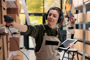 Supervisor wearing headset listening music during inventory in warehouse, scanning cardboard box barcode using store scanner. Storage room manager preparing customers orders working at shipping