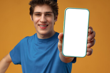 Young delivery man showing smartphone with blank screen in studio