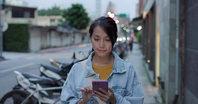 Woman use mobile phone and walk in the street in the evening