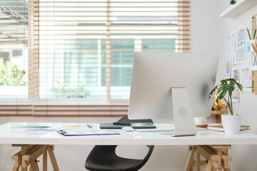 Modern home office interior with computer monitor, books, houseplant and stationery on white table.