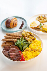 Tenderloin beef steak with scrambled eggs, rocket leaves and potatoes with a side of rye bread.