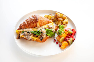 Mediterranean scrambled egg croissant sandwich with fruits and potatoes.