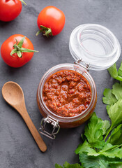 Homemade tomato sauce for pizza or pasta in a jar on a gray background with fresh vegetables and herbs close up.